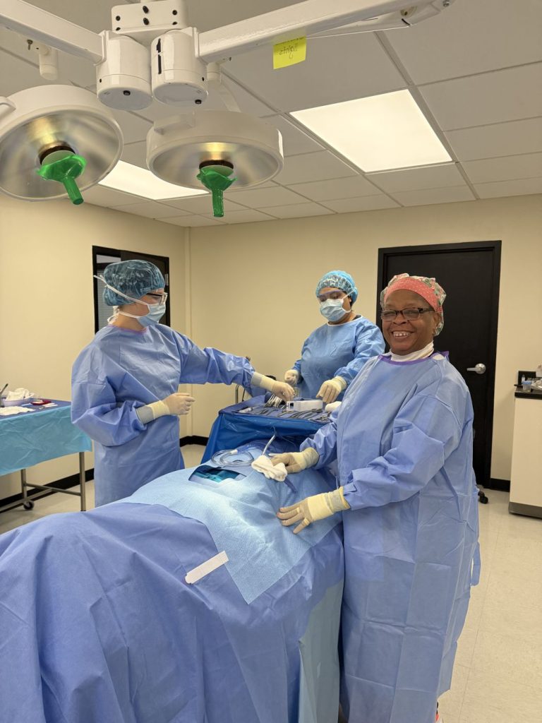 Surgical tech students working at the operating table under surgical lights