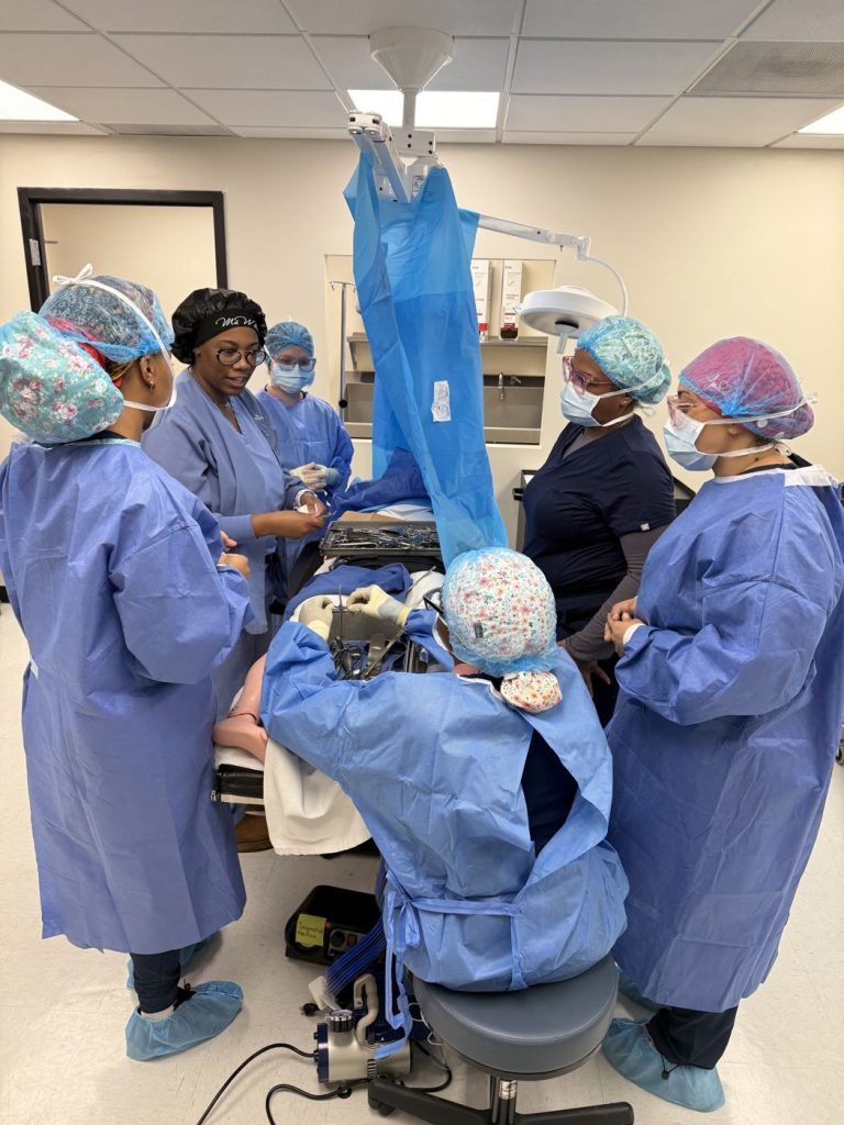 Team of surgical tech students in gowns working around the operating table